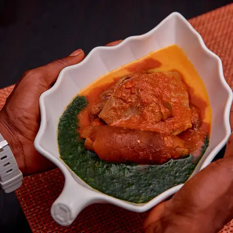 Mãos a segurar um prato de carne guisada com verduras