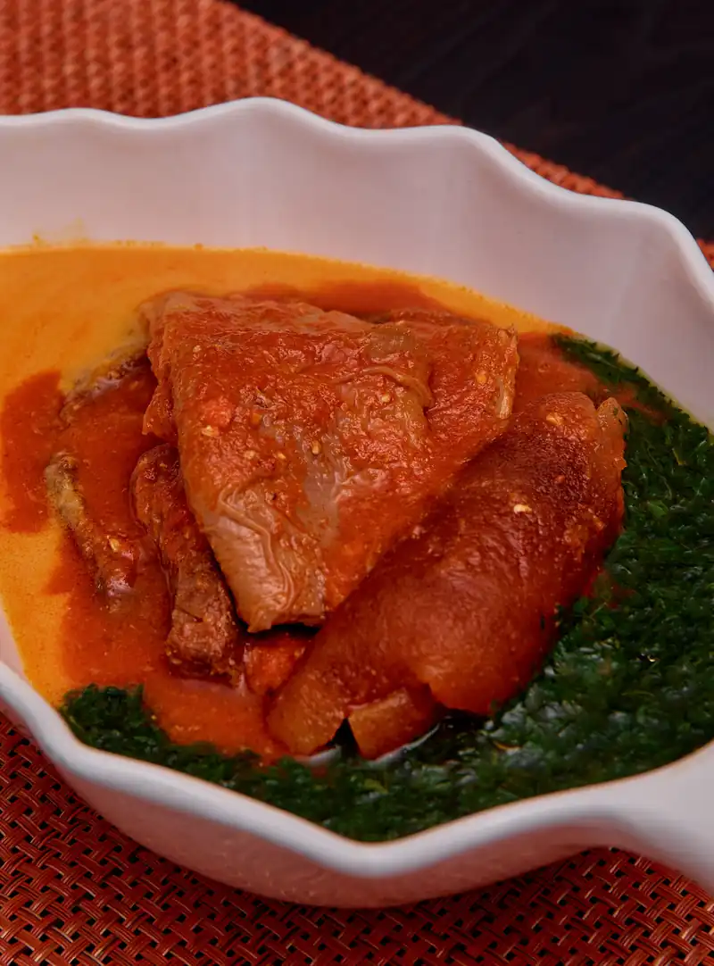 Guisado em molho vermelho de óleo de palma, sobre folhas verdes, numa taça branca
