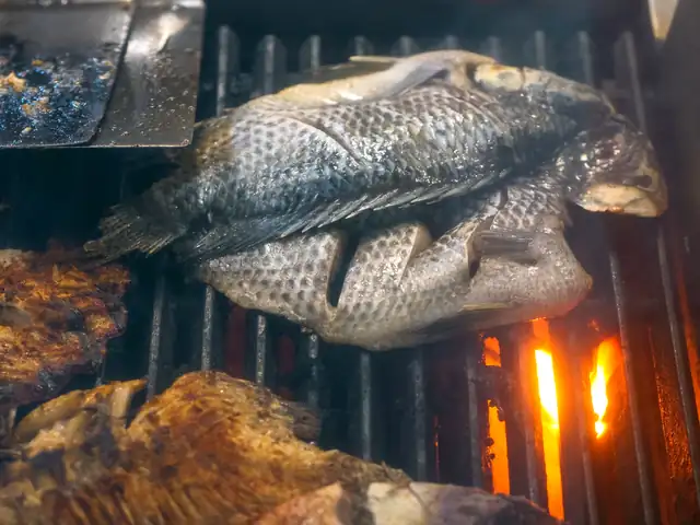 Peixe inteiro a grelhar, com as chamas por baixo da grelha