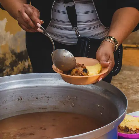 Mão a servir comida de uma panela grande para uma tigela